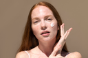 Woman applying cream to her face against a neutral background