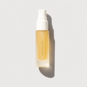 A frosted glass spray bottle containing a golden-yellow liquid, with a white pump dispenser and gold vertical text reading 'ESSENTIAL MIST'. The bottle is centered on a light gray background with a soft shadow cast to the right.