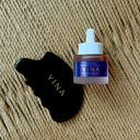 A small bottle of YINA Nourish Botanical serum with a white dropper cap next to a Gua Sha Stone with gold YINA lettering, set on a textured beige woven mat background.