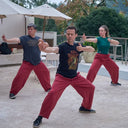 Three people in red pants practising Qigong outdoors.