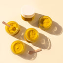 Five jars of YINA Recovery Body Treatment on a beige background