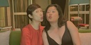 Two women, YINA founders, making kissing faces in a room with a green couch and lampshades.