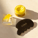 YINA bian‑stone gua sha plate paired with golden Decolletage Body Treatment balm jar